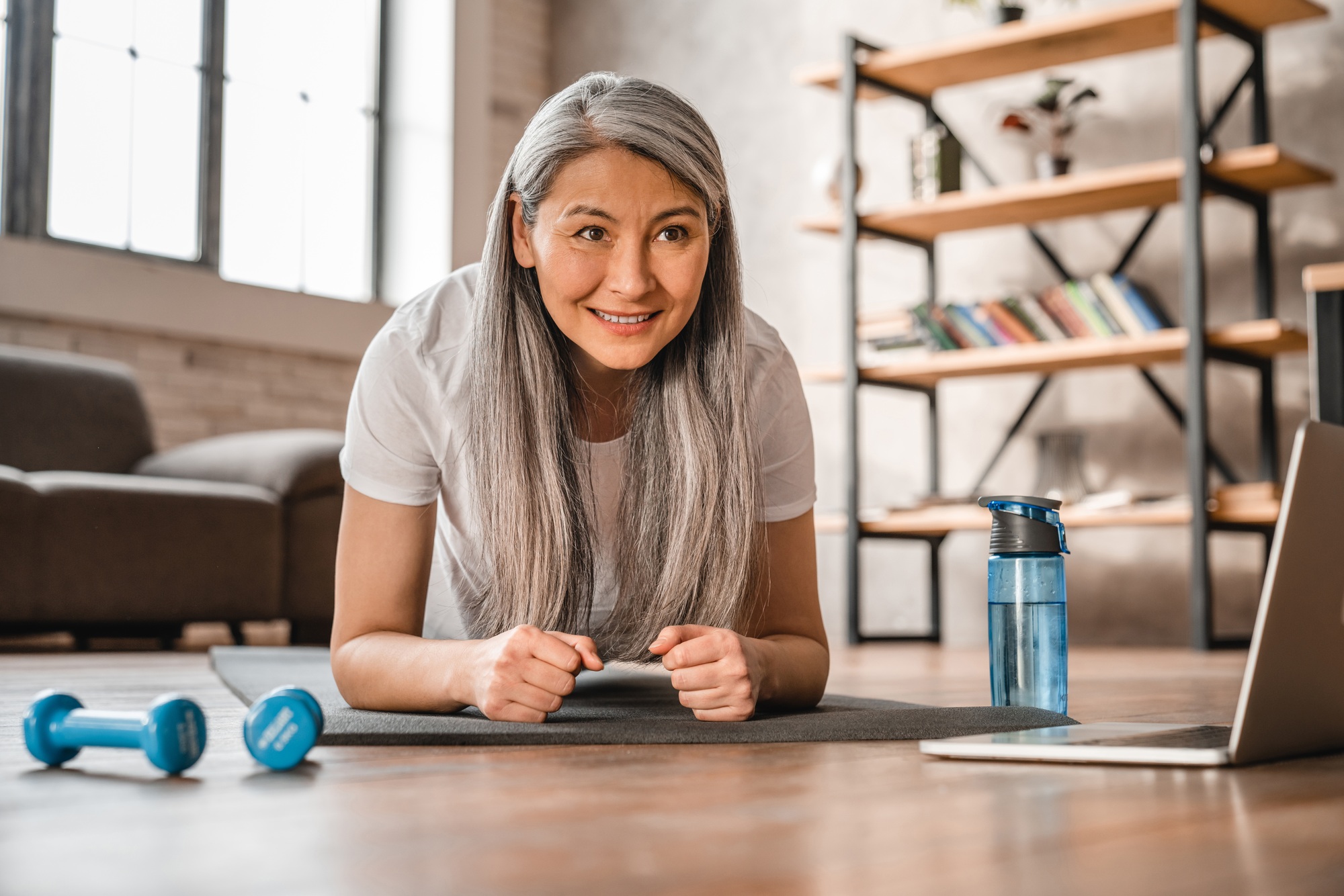 Active mature caucasian lady standing in plank at home with laptop